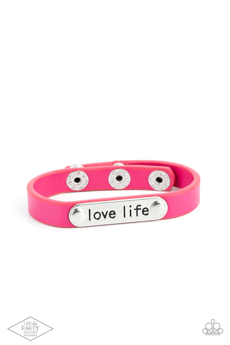 Love Life Pink Wrap Bracelet - Paparazzi Accessories  A silver plate engraved with the inspirational phrase “love life” is studded in place along a skinny strip of pink leather. Brushed in a shiny finish, the dainty band wraps around the wrist for a simple seasonal style. Features an adjustable snap closure.  Sold as one individual bracelet.