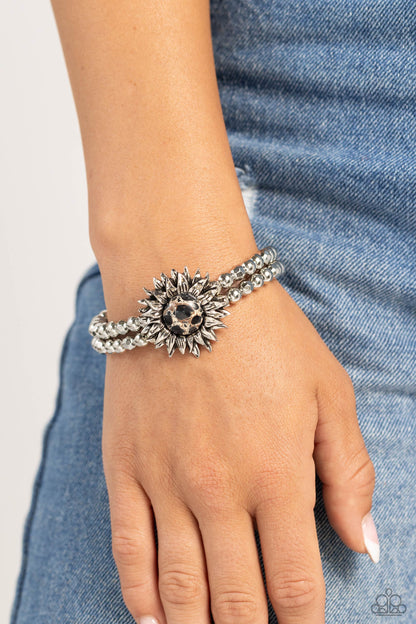 Sunflower Serenity Black Stone Sunflower Stretch Bracelet - Paparazzi Accessories  Strung along elastic stretchy bands, a duo of silver and faceted silver beads wrap around the wrist. Featured atop the beaded collection, an oversized black stone with white marbling is pressed into an intricate-detailed, three-dimensional silver sunflower for a dramatically dazzling finish. As the stone elements in this piece are natural, some color variation is normal.  Sold as one individual bracelet.  P9SE-BKXX-341XX