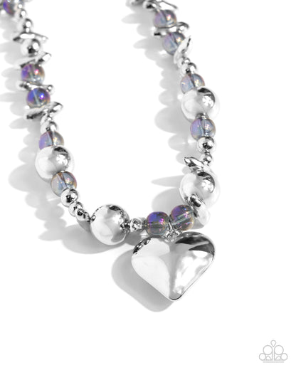 Glistening Gossip Purple Heart Necklace - Paparazzi Accessories Infused along an invisible string, a collection of silver beads in varying sizes, chiseled silver pebbles, and transparent purple iridescent beads loop around the neckline for a glistening display of color. An oversized silver heart pendant swings from the center of the display for a light-hearted finish. Features an adjustable clasp closure. Due to its prismatic palette, color may vary. Includes one pair of matching earrings. P2WH-PRXX-453XX