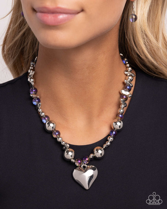 Glistening Gossip Purple Heart Necklace - Paparazzi Accessories Infused along an invisible string, a collection of silver beads in varying sizes, chiseled silver pebbles, and transparent purple iridescent beads loop around the neckline for a glistening display of color. An oversized silver heart pendant swings from the center of the display for a light-hearted finish. Features an adjustable clasp closure. Due to its prismatic palette, color may vary. Includes one pair of matching earrings. P2WH-PRXX-453XX