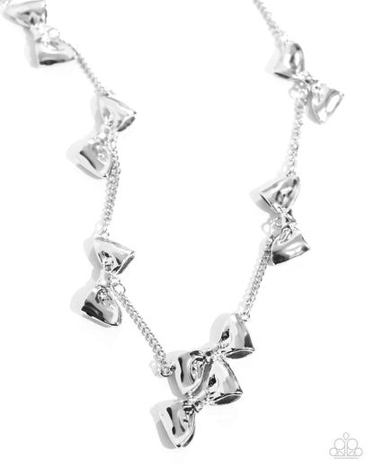 Dapper Definition Silver Bow Necklace - Paparazzi Accessories  Connected along a classic silver chain, a collection of high-sheen, reflective silver bows stand out along the neckline for a dazzling, dapper display. Features an adjustable clasp closure.  Sold as one individual necklace. Includes one pair of matching earrings.   Get The Complete Look! Earring: "Dapper Dalliance - Silver" (Sold Separately)