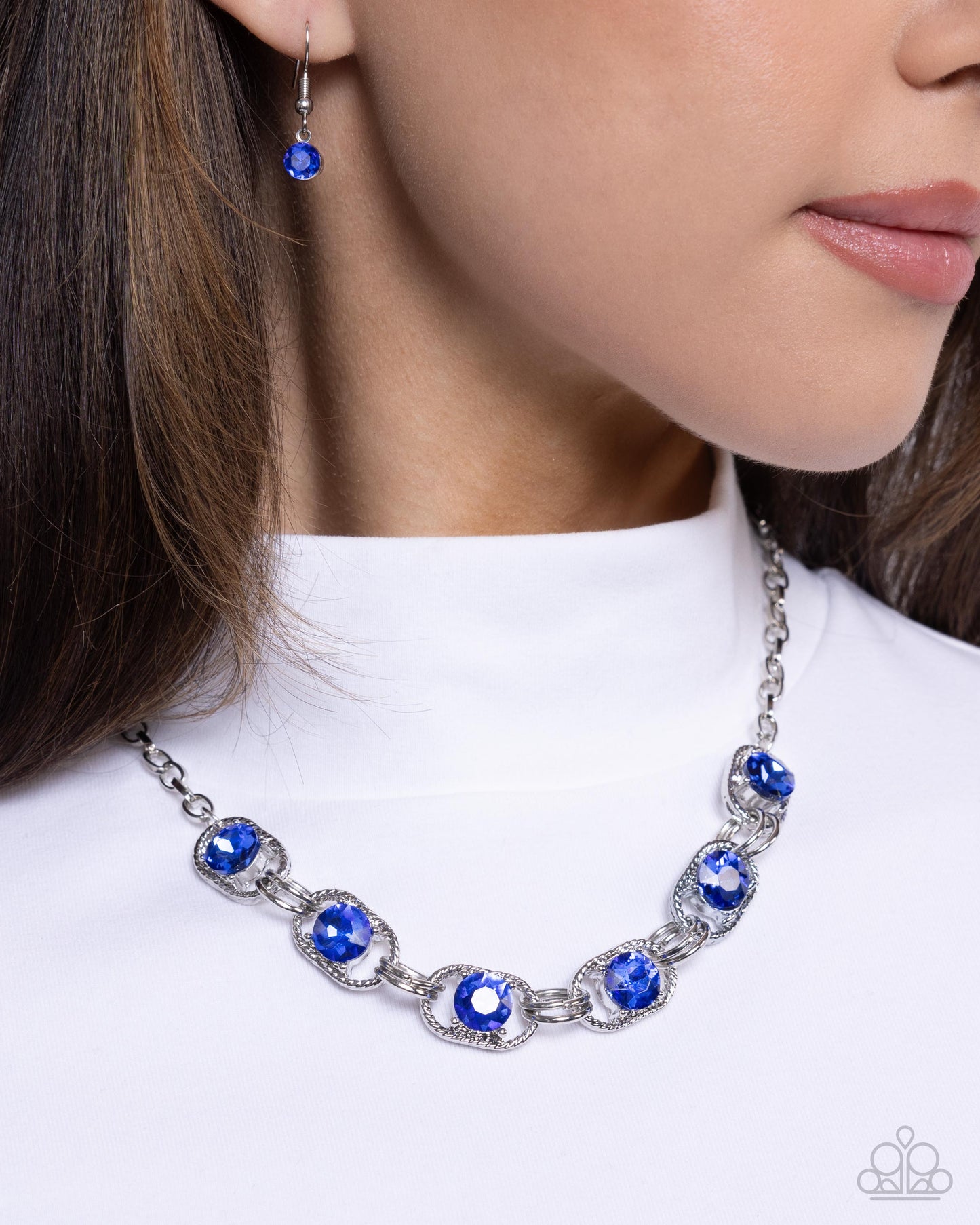 Serrated Sensation Blue Rhinestone Necklace - Paparazzi Accessories  Set in the center of serrated silver links, a collection of faceted Capri Blue gems link below the neckline by duos of silver rings along a silver cable chain for a shimmery sensational statement. Features an adjustable clasp closure.  Sold as one individual necklace. Includes one pair of matching earrings.  P2RE-BLXX-443YF