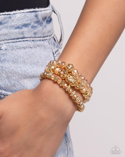 Malibu Maiden Gold Stretch Bracelet - Paparazzi Accessories  Faceted gold clear and opaque beads, various gold beads, and a vintage-embellished oversized bead stack up the wrist on elastic stretchy bands for a classically colorful look.  Sold as one set of three bracelets.  P9BA-GDXX-134XX