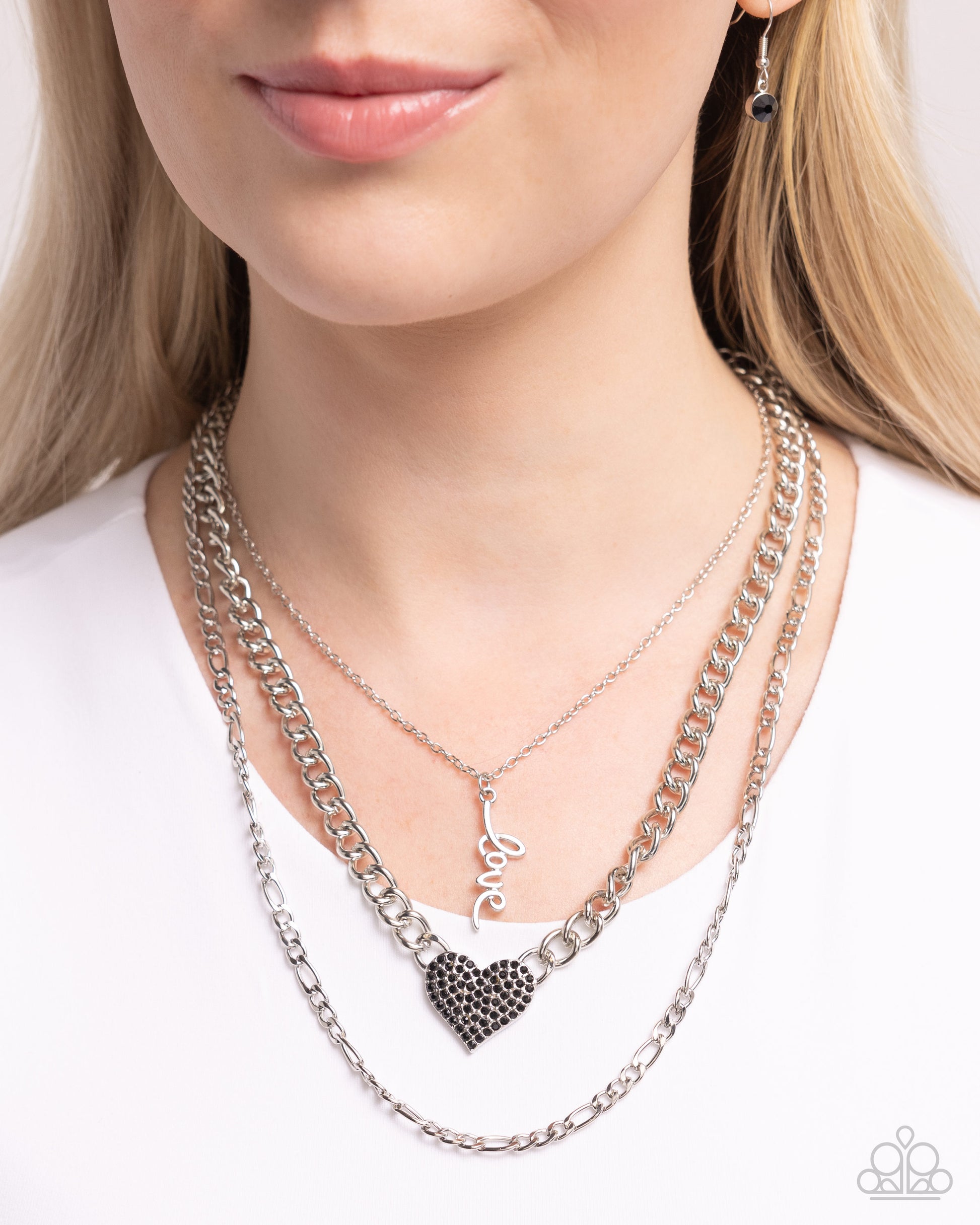 Luxurious Love Black Necklace - Paparazzi Accessories  Three mismatched silver chains loop and layer below the neckline. Featured on the uppermost chain, set in a curly cursive font, silver letters spell out the word "love" while the centermost chain features a black rhinestone-encrusted heart for a romantic radiant display. Features an adjustable clasp closure.  Sold as one individual necklace. Includes one pair of matching earrings.  P2RE-BKXX-488XX