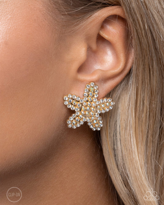 Starfish Serenade Gold Clip-On Earring - Paparazzi Accessories  Embellished in glistening white rhinestones and iridescent rhinestones, a gold starfish glistens from the ear for a shimmery sea-inspired serenade. Earring attaches to a standard clip-on fitting. Due to its prismatic palette, color may vary.  Sold as one pair of clip-on earrings.  P5CO-GDXX-089XX