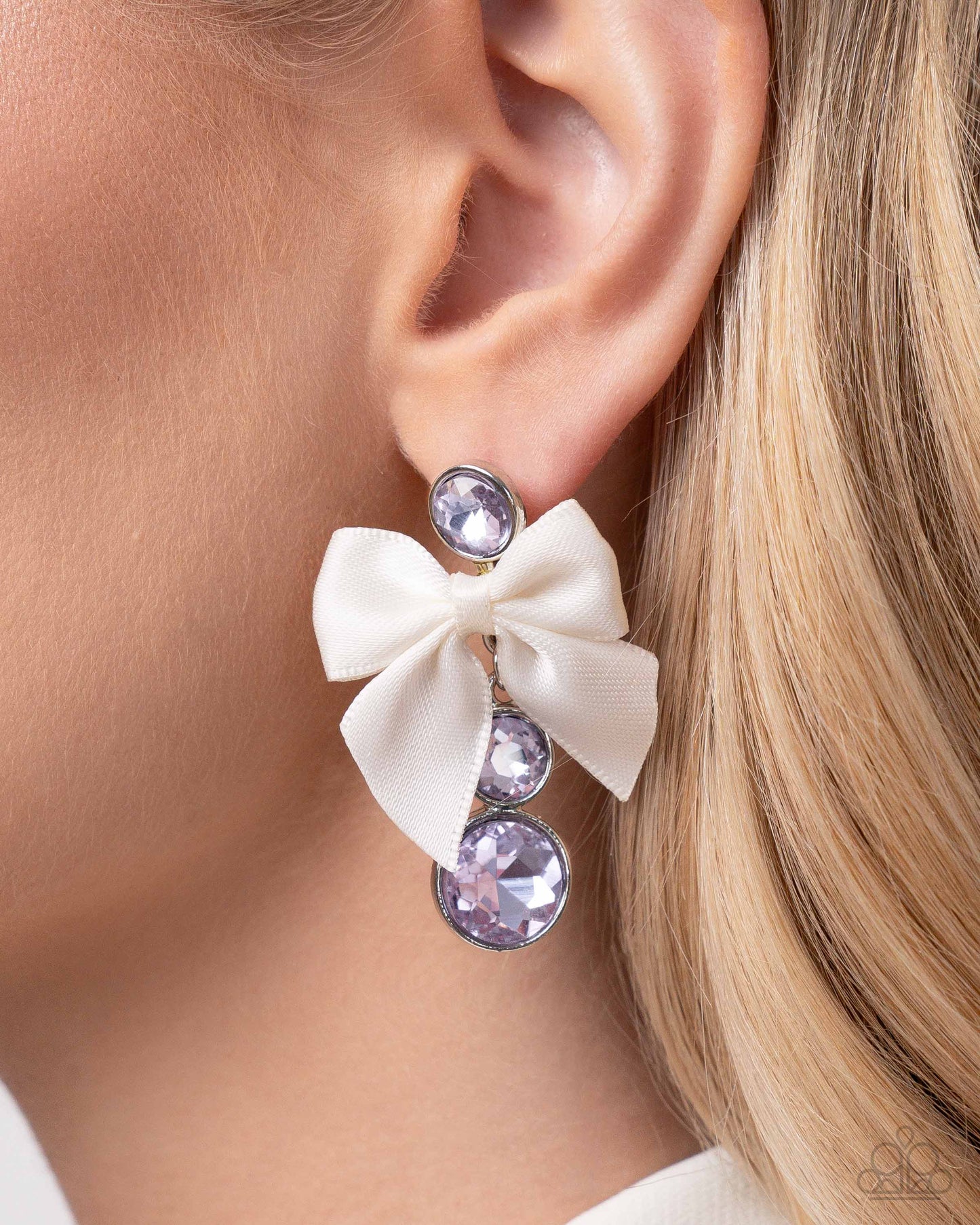 Genteel Glam Purple Post Earring - Paparazzi Accessories  Three timeless violet gems in varying sizes are delicately encased in silver frames as they link below the ear into a refined lure. An ivory bow is tied along the glittery strand between two gems, adding a layer of sophistication to the glamorous look. Earring attaches to a standard post fitting.  P5PO-PRXX-037BF  Sold as one pair of post earrings.&nbsp;  Get The Complete Look! Necklace: "Genteel Gallery - Purple" (Sold Separately)