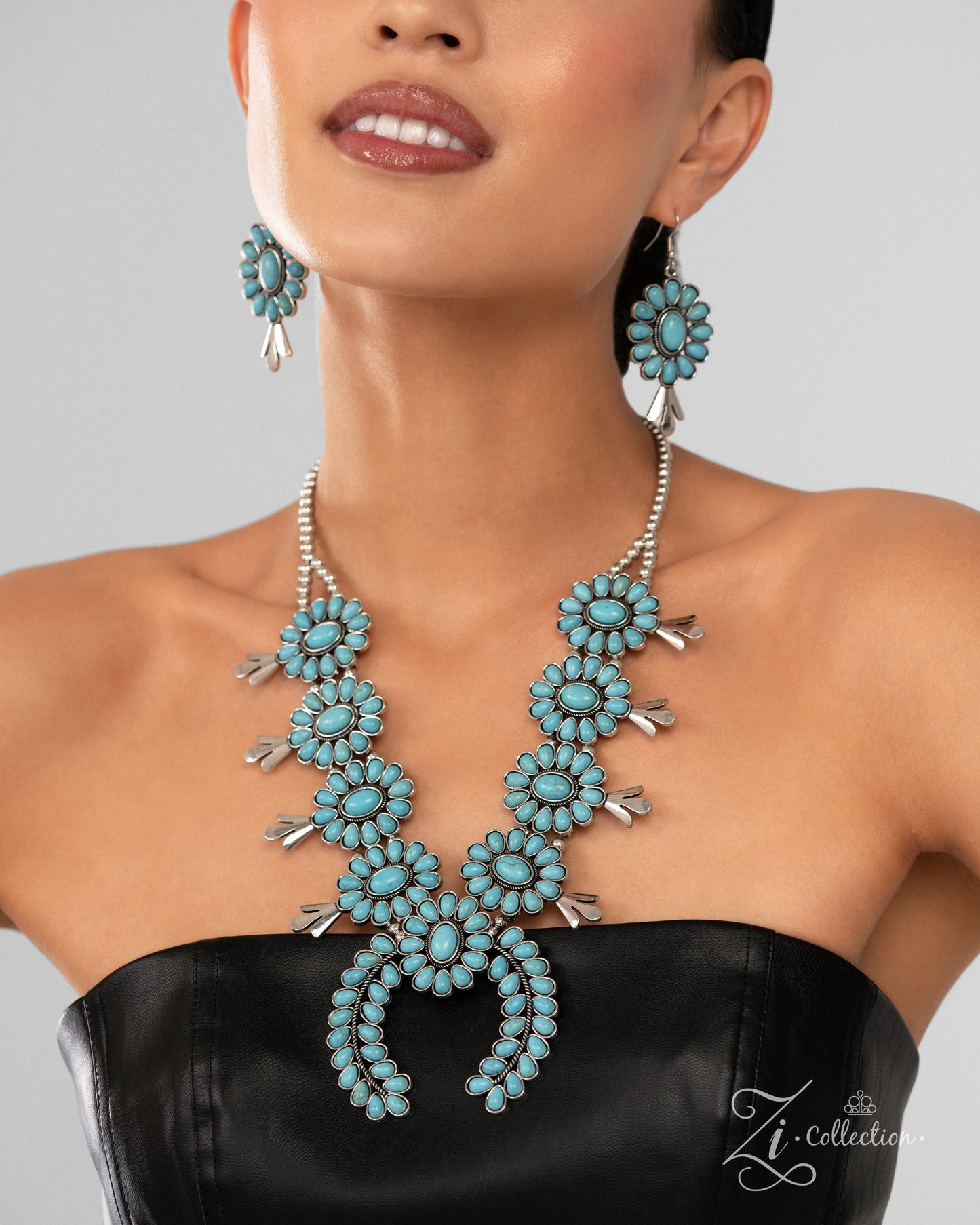 The Shelby Turquoise 2024 Zi Necklace - Paparazzi Accessories  Item #Z2409  A collection of turquoise stone-embellished squash blossom frames, with an oversized crescent-shaped pendant at its center, cascades below the neckline from a strand of silver beads that split into two distinct strands. The vibrant splashes of color and antiqued rope-textured centers of the squash blossom frames infuse the rustic design with a hint of surprising whimsicality and traditional timelessness. Features an adjustable clasp