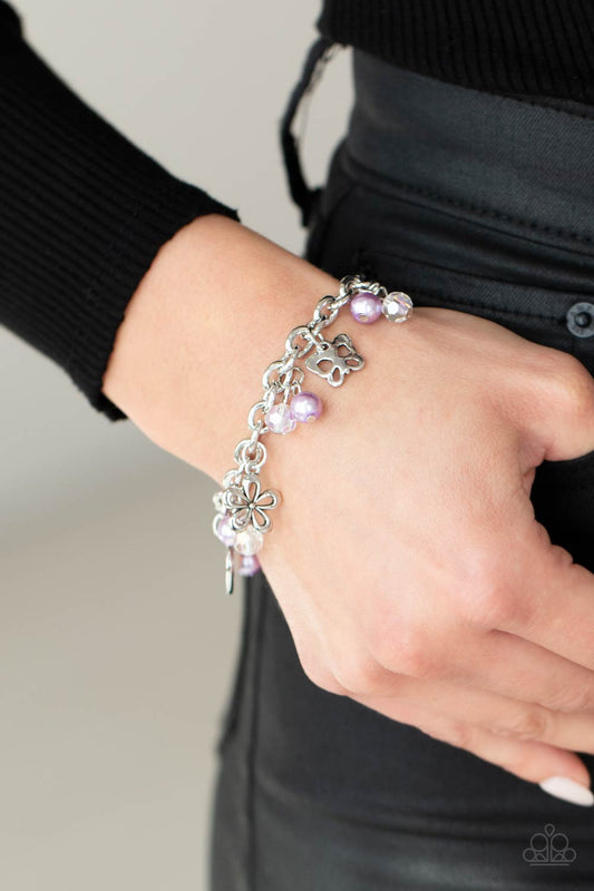 Retreat into Romance Purple Charm Bracelet - Paparazzi Accessories.  Infused with purple pearls and iridescent crystal-like beads, mismatched silver charms including a clover, butterfly, heart, and floral frames swing from a chunky silver chain around the wrist. Features an adjustable clasp closure.  ﻿All Paparazzi Accessories are lead free and nickel free!  Sold as one individual bracelet.