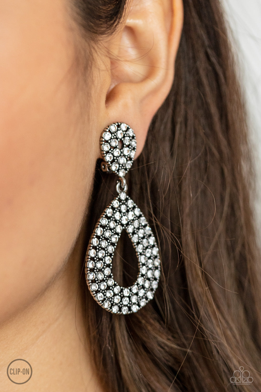 Pack In The Pizzazz White Clip-On Earring - Paparazzi Accessories  A white rhinestone encrusted silhouette teardrop attaches to the bottom of a dainty white rhinestone encrusted teardrop, creating a glamorous lure. Earring attaches to a standard clip-on fitting.  Sold as one pair of clip-on earrings.