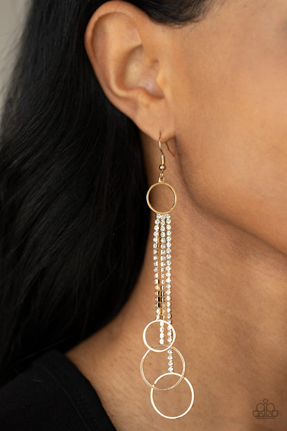 Demurely Dazzling Gold Earring - Paparazzi Accessories  Dainty gold hoops swing from the bottom of glittery strands of glassy white rhinestones that attach to the bottom of a dainty gold ring, creating a tantalizing tassel. Earring attaches to a standard fishhook fitting.  Sold as one pair of earrings.