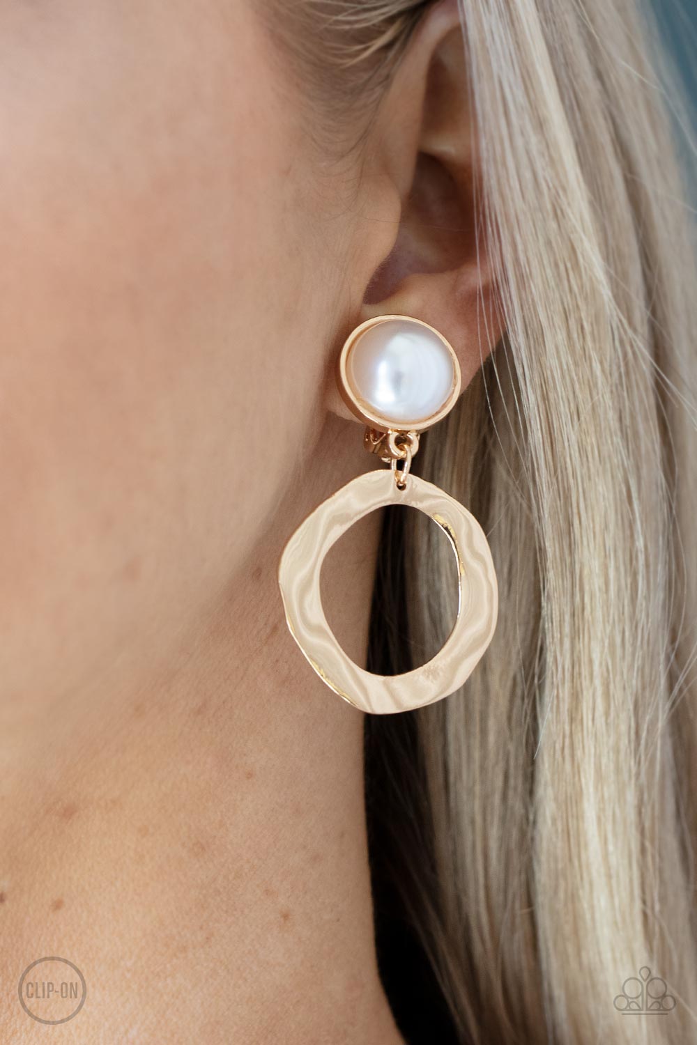 Vintage Veracity Gold Clip-On Earring - Paparazzi Accessories  Delicately hammered in light-catching shimmer, an asymmetrical gold hoop swings from the bottom of an oversized pearl-drop fitting for a vintage flair. Earring attaches to a standard clip-on fitting.  Sold as one pair of clip-on earrings.