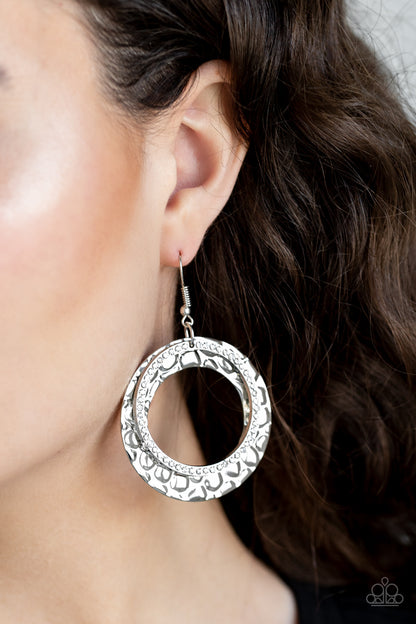 Cinematic Shimmer White Earring - Paparazzi Accessories Item #E108 Encrusted in glassy white rhinestones, a glittery silver hoop links with a thick silver hoop embossed in metallic pebble-like patterns, creating a refined lure. Earring attaches to a standard fishhook fitting. All Paparazzi Accessories are lead free and nickel free!  Sold as one pair of earrings.