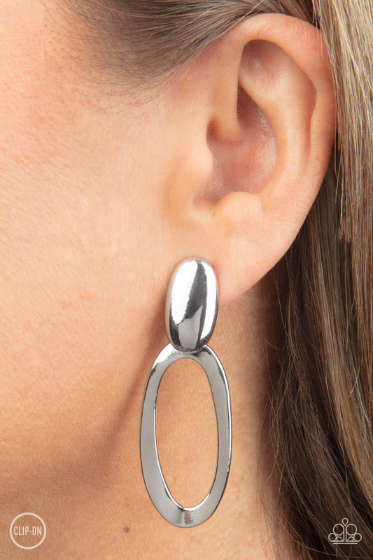 Pull OVAL! Silver Clip-On Earring - Paparazzi Accessories  An asymmetrical silver oval hinges from the bottom of a spherical silver oval fitting, resulting in a radiant lure. Earring attaches to a standard clip-on fitting.  Sold as one pair of clip-on earrings.  P5CO-SVXX-109XX