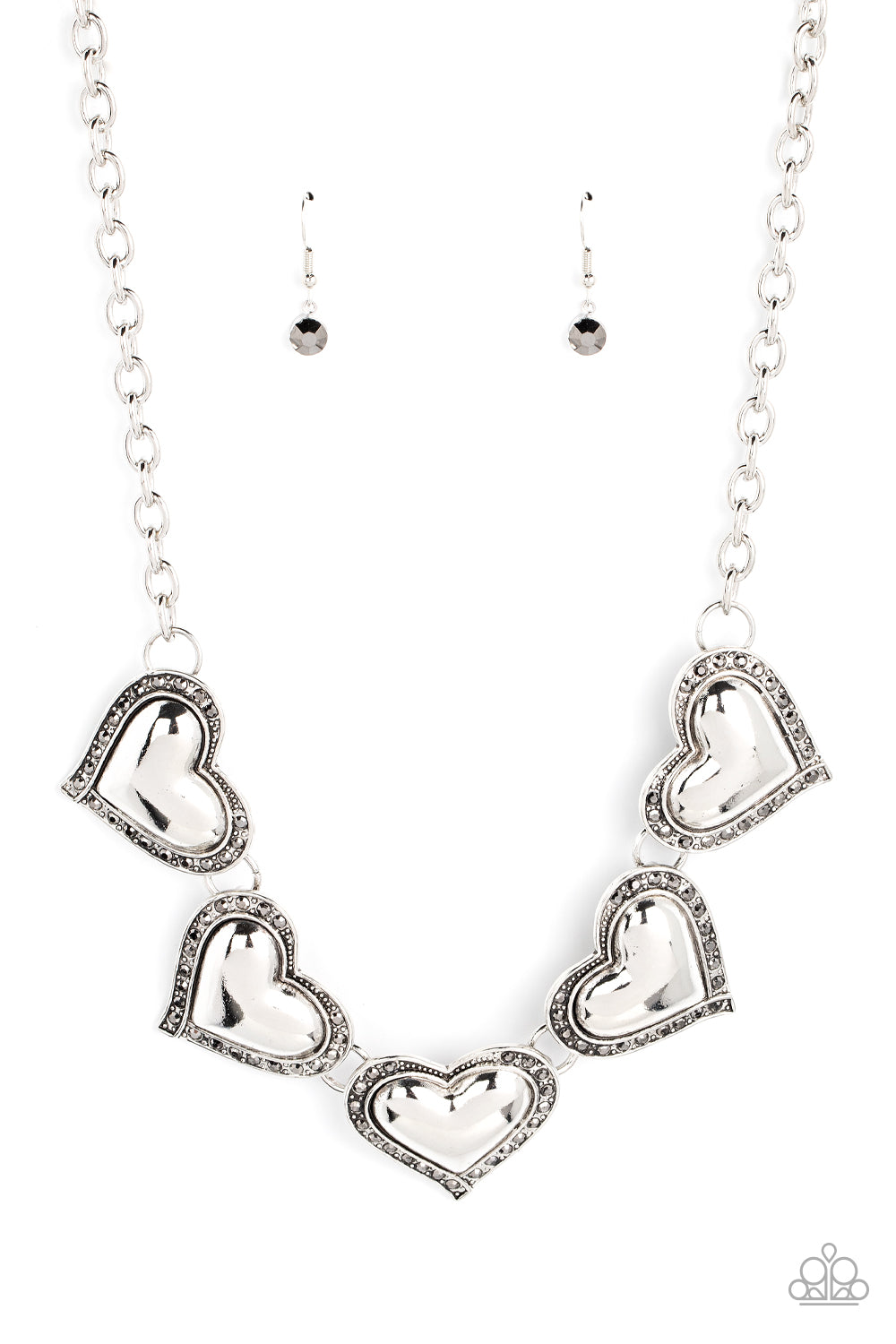 Kindred Hearts Silver Necklace - Paparazzi Accessories  Bordered in glitzy hematite rhinestones, an oversized collection of beveled silver heart frames delicately links below the collar for a dramatically romantic look. Features an adjustable clasp closure.  Sold as one individual necklace. Includes one pair of matching earrings.