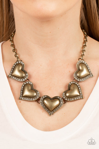 Kindred Hearts - Brass Item #P2WH-BRXX-173XX Bordered in glassy white rhinestones, an oversized collection of beveled brass heart frames delicately links below the collar for a dramatically romantic look. Features an adjustable clasp closure.  Sold as one individual necklace. Includes one pair of matching earrings.