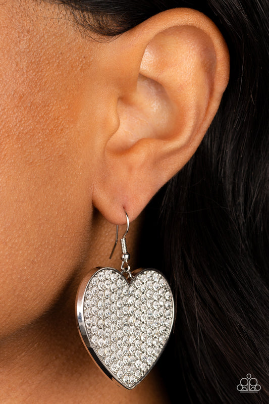 Romantic Reign White Earring - Paparazzi Accessories  A shiny, oversized silver heart is covered in tiny white rhinestones, emitting radiant shimmer as it swings from the ear. Earring attaches to a standard fishhook fitting.  Sold as one pair of earrings.