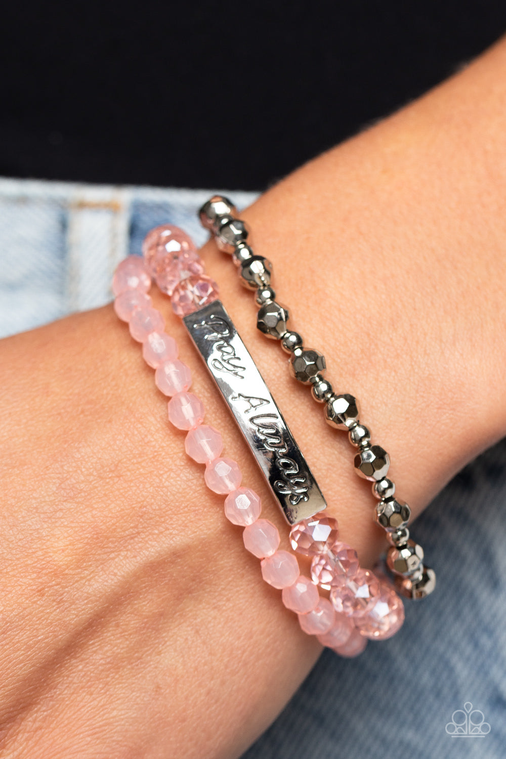 Pray Always Pink Bracelet - Paparazzi Accessories  Varying in shape and shimmer, faceted silver beads, milky pink beads, and glittery pink crystal-like beads are threaded along elastic stretchy bands, creating colorful layers across the wrist. Featured on the crystal-like band, a curved silver bar features the words "Pray Always" in a curly, stamped font for a soft finish.  Sold as one individual bracelet.