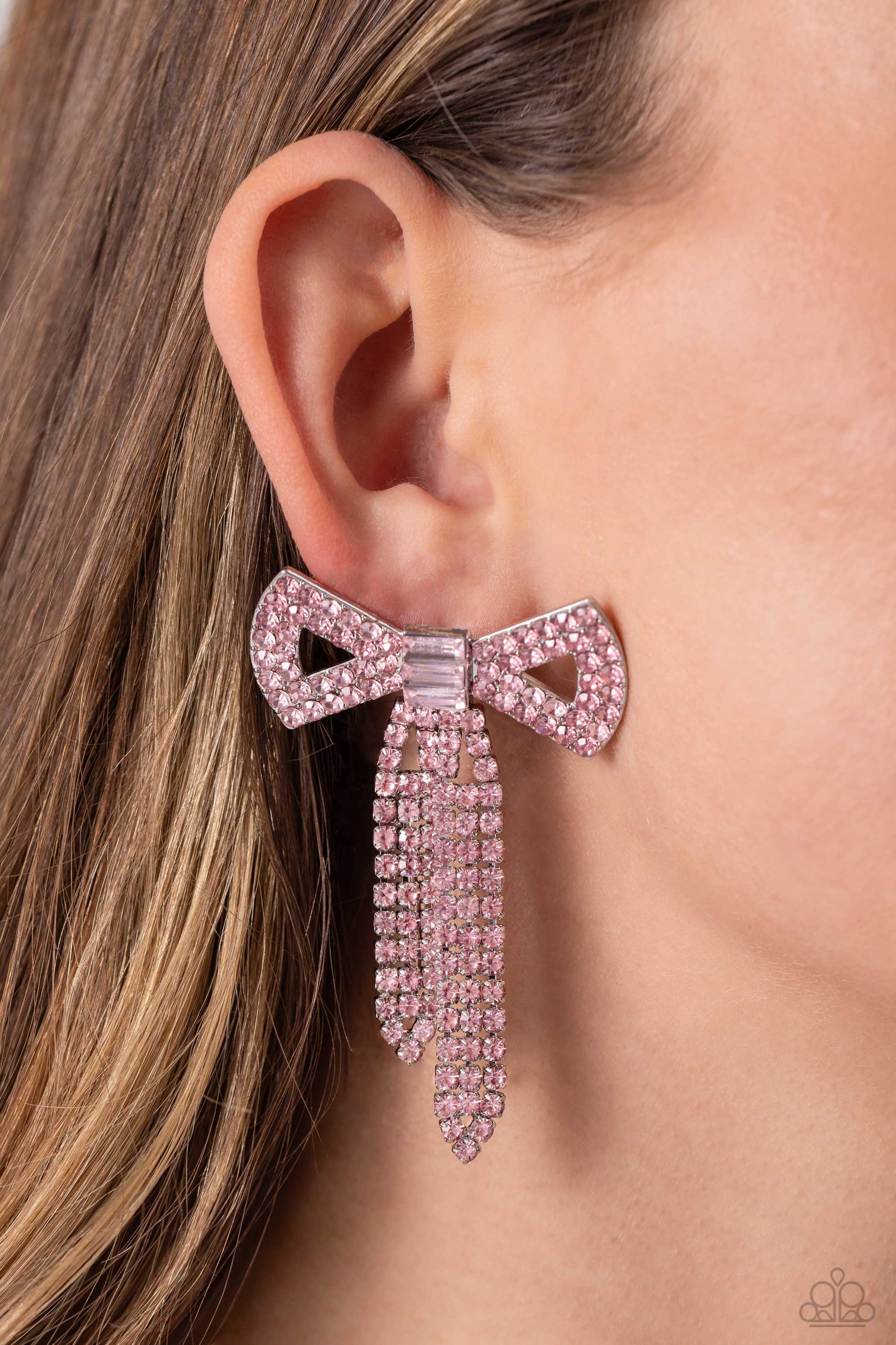 Just BOW With It Pink Post Earring - Paparazzi Accessories  Featuring silver square fittings, high-sheen bands of silver, adorned in sparkling pink rhinestones loop into a stunning bow charm, creating a classy statement at the ear. Featured in the center of the classy design, a trio of emerald-cut pink gems tie the bow together emitting further sheen and glitz. Earring attaches to a standard post fitting.  Sold as one pair of post earrings.  P5PO-PKXX-091XX