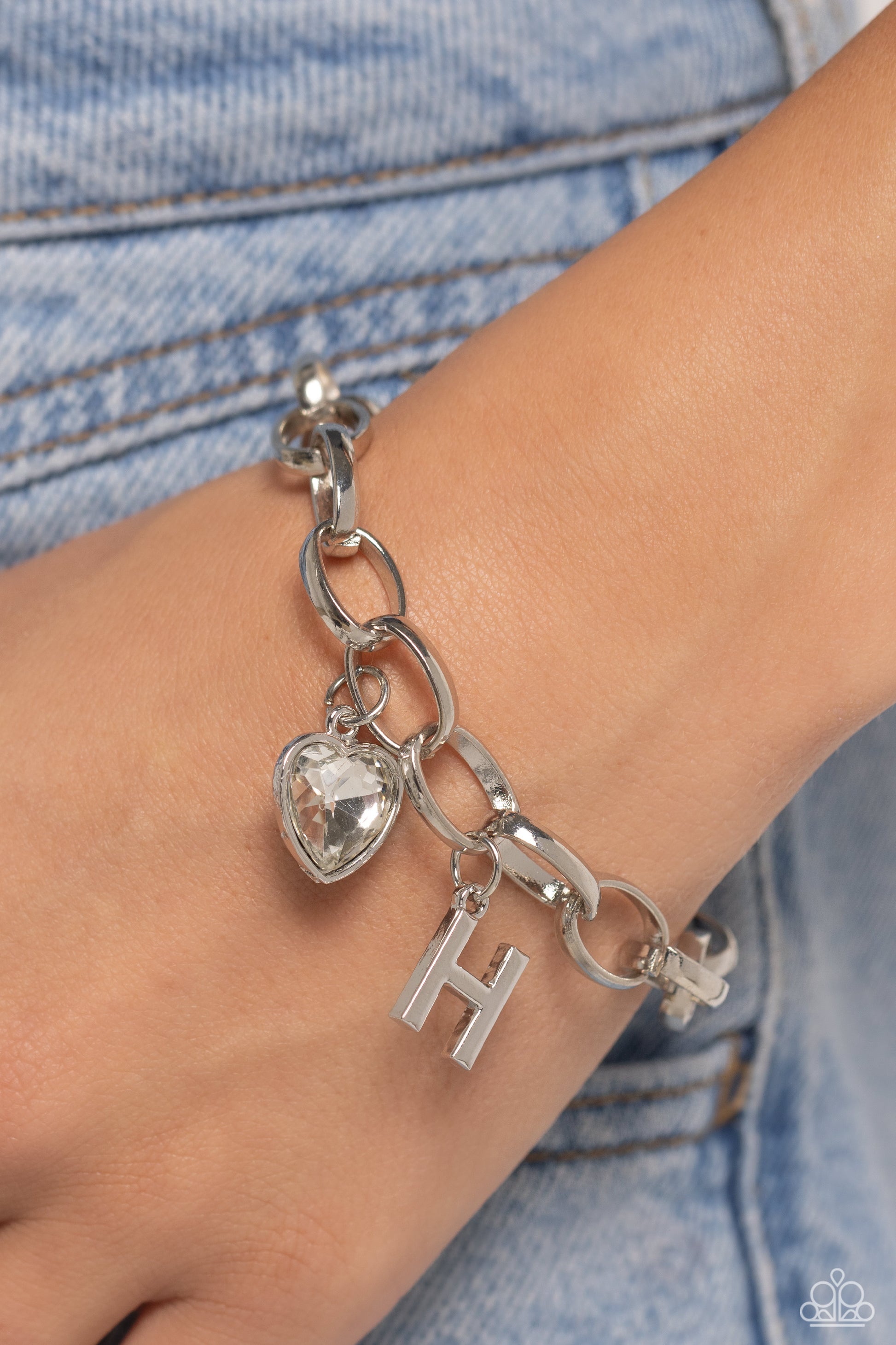 Guess Now Its INITIAL White "H" Bracelet - Paparazzi Accessories  A simple collection of silver charms — including a white rhinestone heart pressed in a silver frame and a sleek letter "H" — dance from a chunky silver chain around the wrist, creating a sentimental fringe. Features an adjustable clasp closure.  Sold as one individual bracelet.  New Kit Sku:  P9BA-WTXX-042XX